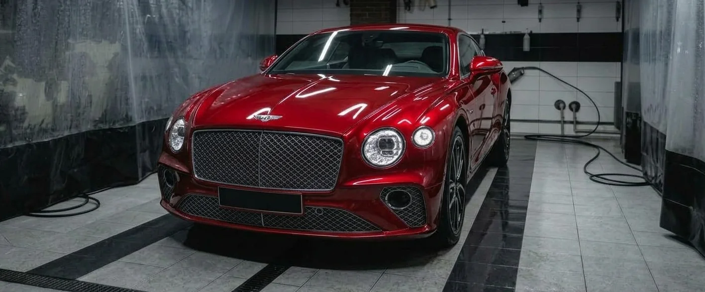 A freshly washed red luxury car with its headlights on in a tiled wash bay
