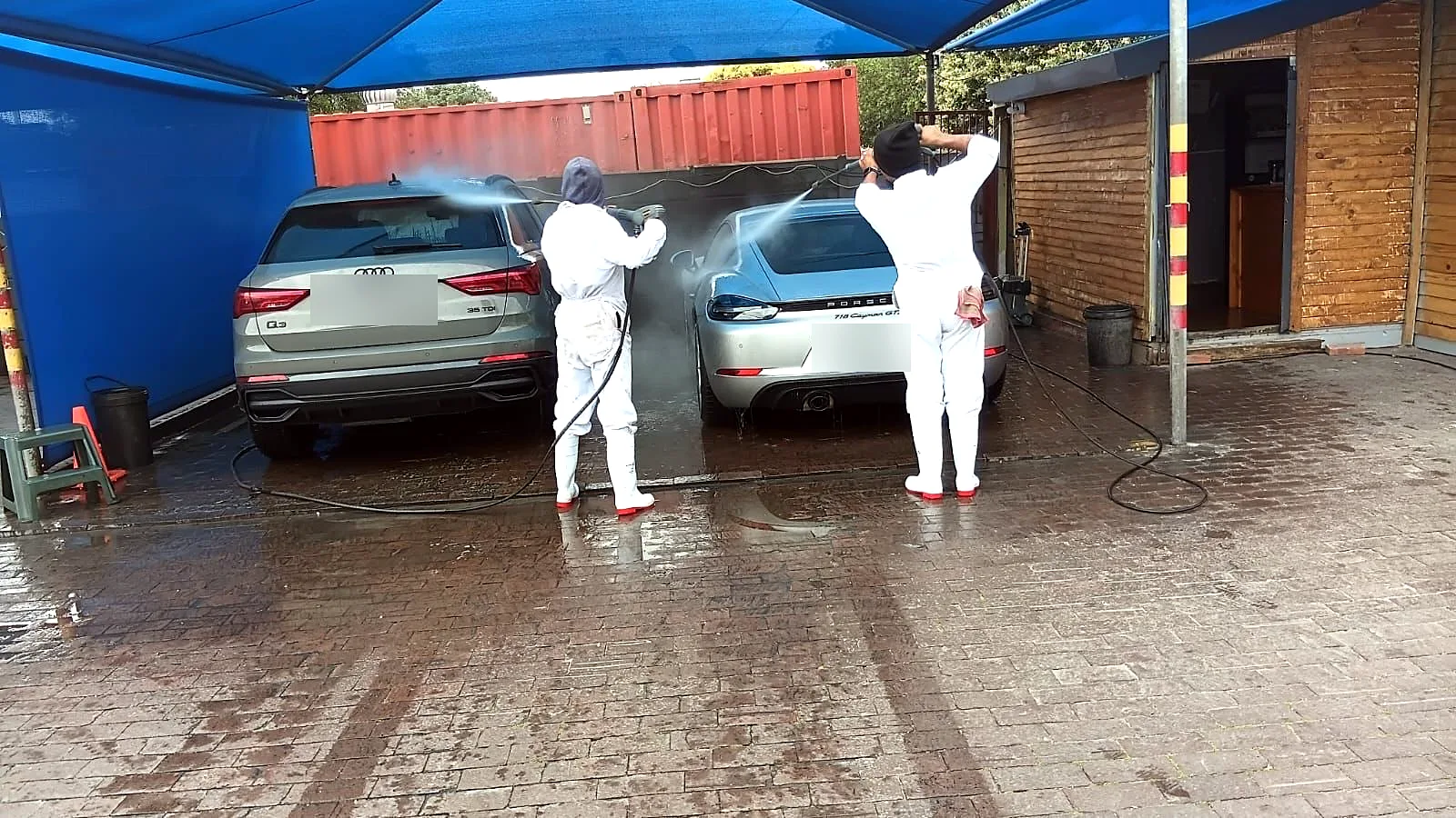 Two Melkbos Auto Spa detailers rinsing an Audi and a Porsche in the wash bay